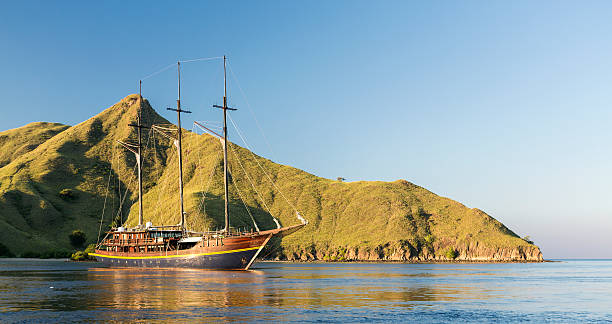 A wooden yacht with three masts is anchored in the waters of the famous archipelago of Komodo in Indonesia. The National Park of Komodo attracts numerous diving expeditions as it is considered one of the best diving destination in the World.
