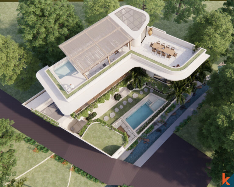 An aerial view of a luxurious, modern villa with a unique curved design, featuring a rooftop terrace, an outdoor dining area, and a private swimming pool surrounded by lush gardens and tropical trees. The property exemplifies contemporary architectural style integrated with natural surroundings